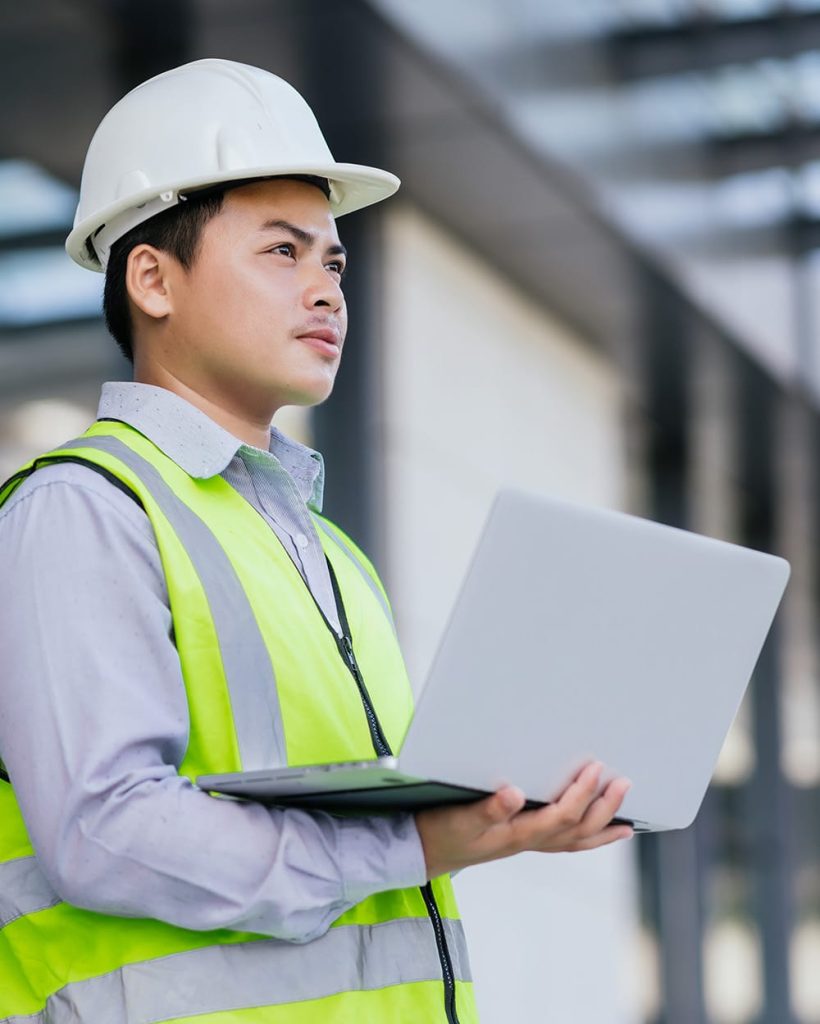 asian-engineer-young-man-wearing-safety-vest-helmet-standing-using-computer-check-work-building-construction-site-background-engineering-construction-worker-concept